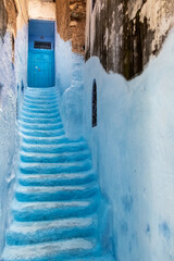 In the medina of Chefchaouen in Morocco. A narrow staircase painted in blue climbs between 2 walls to a closed blue door