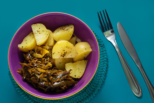 Uma tigela de carne de casca de banana e batatas cozidas, temperadas e prontas para comer em uma superfície verde.