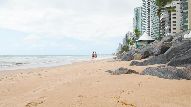 View of the beach and people doing morning walk at the sand of a seaside town. Beach of Boa Viagem, Recife, PE, Brazil.