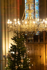 A chandelier in a church with a decorated Christmas tree in the background
