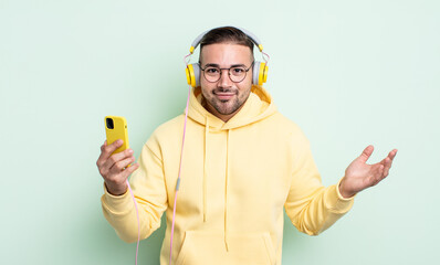 young handsome man feeling puzzled and confused and doubting. headphones and smartphone concept