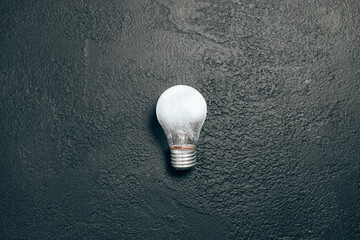 Single white light bulb idea on a dark grunge blackboard background. Creative inspiration, planning ideas concept. Flat lay, top view, copy space
