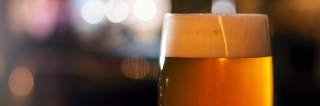 full glass of beer on blurred lights background panorama