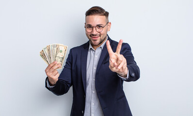 young handsome man smiling and looking friendly, showing number two. dollar banknotes concept