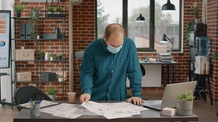 Portrait of businessman with face mask working on project strategy and planning. Engineer designing papers with data charts and analysis to create presentation during covid 19 pandemic. - Powered by Adobe