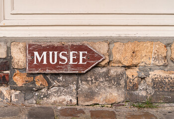 Old used wooden Museum direction sign in french on the antique brick facade