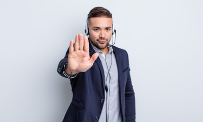 young handsome man looking serious showing open palm making stop gesture. telearketer concept