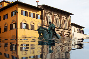 Mediterranean square with village houses and statue in floodwater. Road with overflown water....