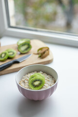 Oatmeal with kiwi and honey in a white bowl on a table. Tasty and healthy breakfast.