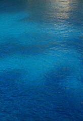 Türkisblaues Meer mit helleren und dunkleren Bereichen und goldener Reflexion Hochformat