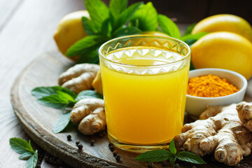 Immune booster antivirus drink, turmeric with ginger, lemon, mint and spices hot winter tea on wooden rustic background, closeup, natural medicine and naturopathy concept