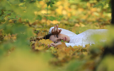 autumn portrait of a beautiful brunette lying on the grass with leaves