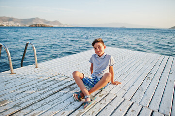 Fototapeta na wymiar Boy sit at Turkey resort on pier against Mediterranean sea.