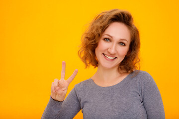 Young happy woman with curly hair standing over yellow background smiling with happy face looking and pointing to the side with thumb up. Place for your text