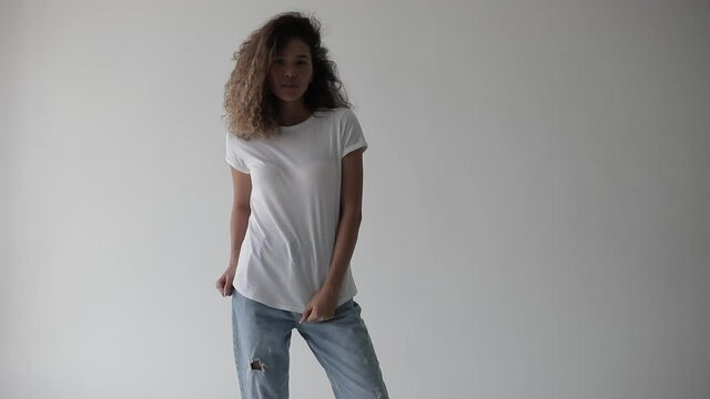 Woman with curly hair in a white t-shirt posing on a white background.