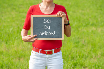 Frau auf einer Wiese mit einer Tafel auf der 