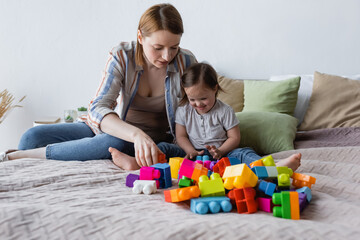 Woman and child with down syndrome playing building blocks on bed at home.