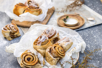 Obraz na płótnie Canvas Closeup of fresh homemade cinnamon buns with frosting in basket surrounded by baking ingredients