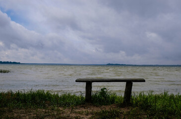 Handicraft wooden empty bench on the shore. Storm lake background.