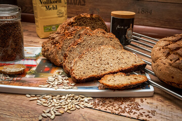 Side view of sliced homemade brown-golden whole wheat bread surrounded by ingredients including bag of flour with 
