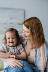 Smiling mother hugging daughter with down syndrome in bedroom.