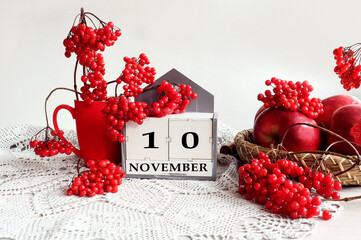 Calendar for November 10: the name of the month in English, the number 10, a bouquet of viburnum and viburnum branches, apples on a tray on a gray openwork napkin, gray background