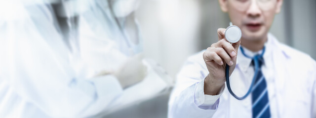 Senior doctor wearing white coat standing to show stethoscope in his hands with copy space in banner size with double exposure nurse blur background. Medical equipment ready to listen lungs or heart