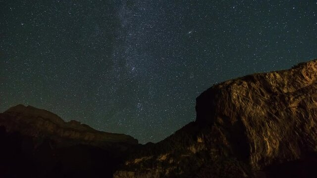 Milky Way and Andromeda Galaxy move over nightsky with rock formation in foreground, Torla, Spain