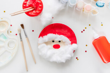 The child glues the parts Santa made from paper plate. Handmade. Project of children's creativity, handicrafts, crafts for kids. Preparation for christmas. Decoration.