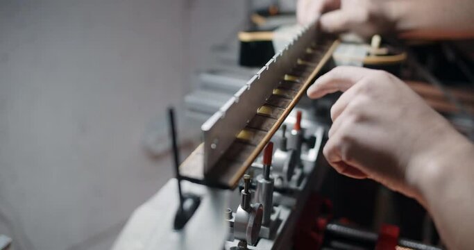 Luthier adjusts the fretboard angle in the electric guitar mounted on the jig, repairing the musical instruments at hte shop, 4k 60p 10 bit