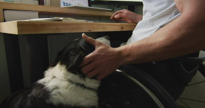 Happy caucasian disabled man in wheelchair using computer in bedroom with his pet dog
