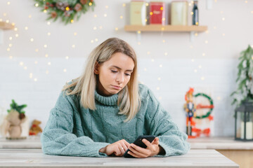 Beautiful lonely depressed woman left alone on Christmas Eve, sadly looking at the phone