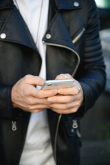 Cropped view of smartphone in hands of stylish man in leather jacket outdoors 