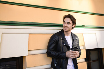 Smiling man in leather jacket holding paper cup near building outdoors 