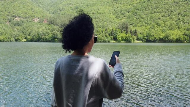 Hiker woman using her phone to check the location and the map while hiking on a mountain near a lake