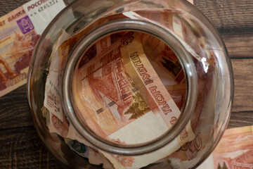 Glass jar stuffed with cash money savings on wooden table close, top view