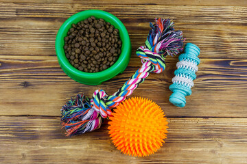 Dog toys and feed for dogs in green plastic bowl on wooden background. Top view. Dog care concept
