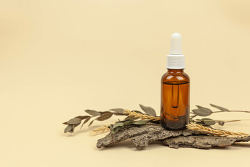A brown bottle with a cosmetic product on a natural beige background made of branches and leaves.