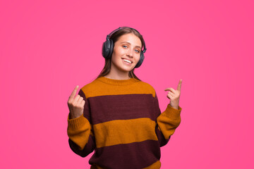 Cute smiling girl is wearing some headphones and pointing up with both hands.