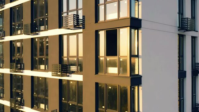 Aerial side view of a newly built modern high-rise apartment building facade. Close-up elevator shot at sunset