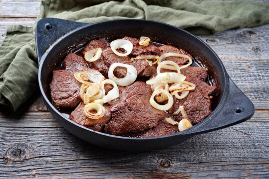Traditional Filipino dry aged angus bistek tagalog steak with onion rings in soy sauce served as close-up in a cast-iron casserole