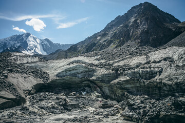 Scenic highlands landscape with big cracked glacier with scratches among moraines on background of high snowy mountain peak and rock top. Awesome scenery with large glacier and great snowy mountain.