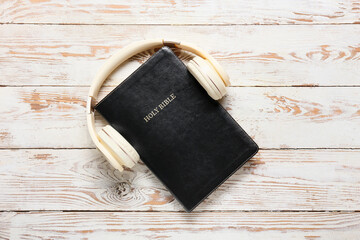 Holy Bible and modern headphones on light wooden background