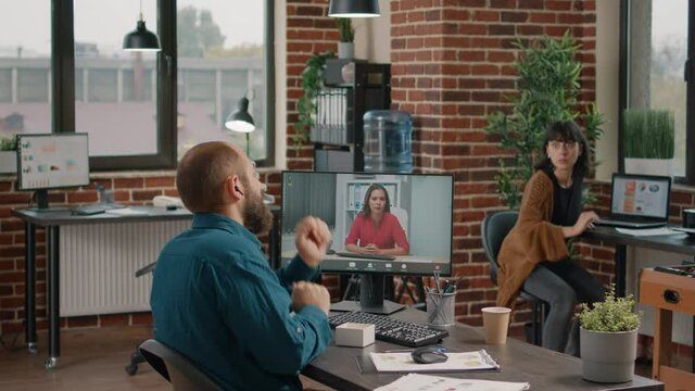 Entrepreneur using earpods to talk to manager on video call in startup office. Business man talking to woman on remote online video conference on computer to plan project and strategy.