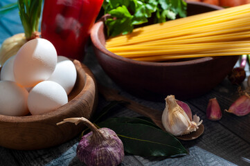 long semolina noodles in a wooden bowl with assorted vegetables eggs on table and light from a...