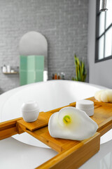 Tray with calla lily and cosmetic bottles on bathtub in room
