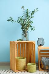 Vase with eucalyptus branches and lamp on wooden boxes near blue wall