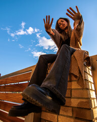 Beauty model girl smiling and posing with a blue sky and brown jacket and black 80's trousers 