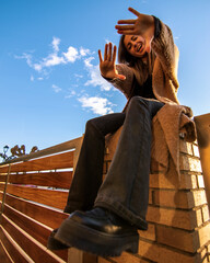 Beauty model girl smiling and posing with a blue sky and brown jacket and black 80's trousers 