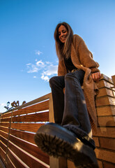 Beauty model girl smiling and posing with a blue sky and brown jacket and black 80's trousers 